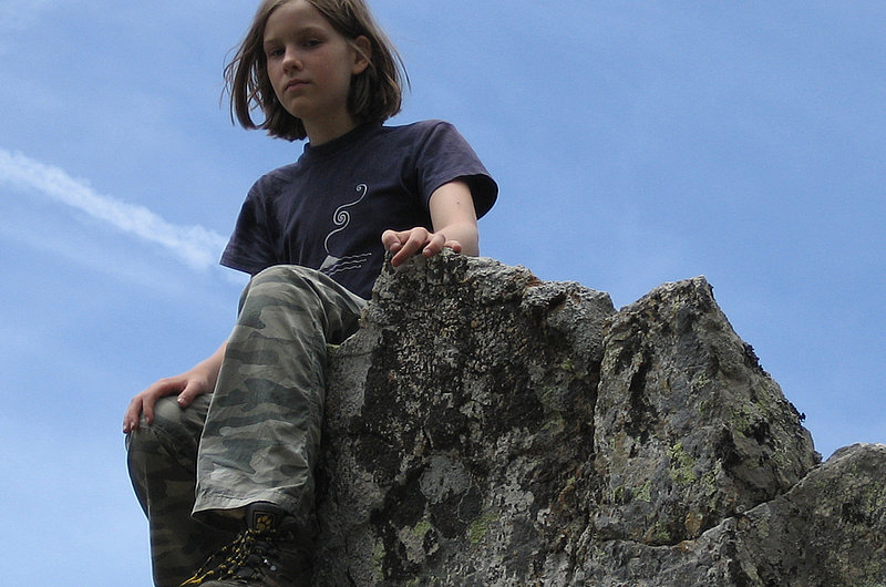 Ein Mädchen in Wanderschuhen sitzt auf einem Felsen und blickt in die Kamera