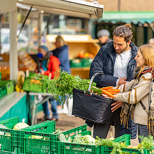 Ein junges Paar kauft frisches Gemüse auf dem Markt ein
